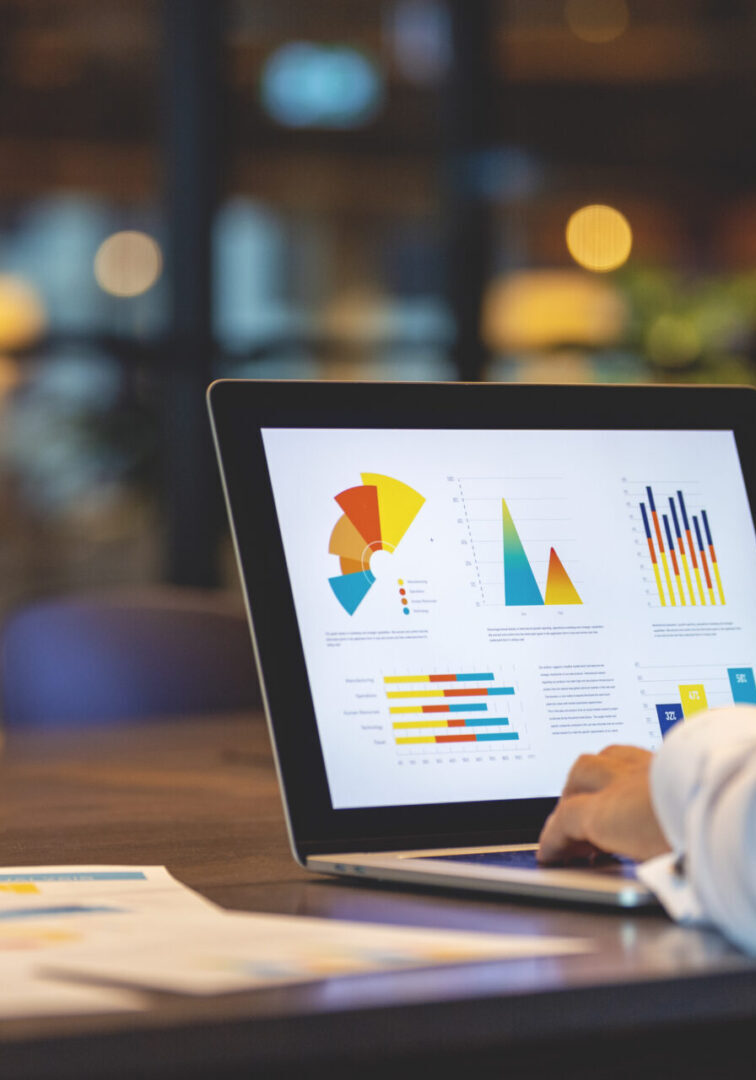Close up of businessman using a laptop with graphs and charts on a laptop computer. Person analyzing colorful charts and graphs on a laptop screen in an office setting. A takeaway coffee cup and papers are on the table.